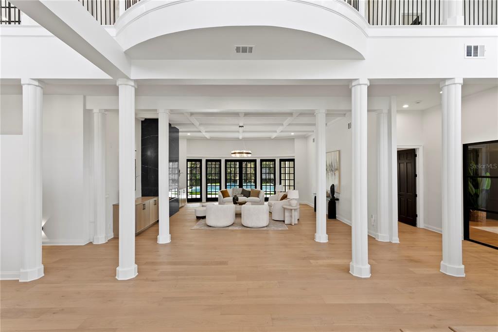 A spacious, open-concept living room features white columns, light wood floors, and black-framed glass doors — 6324 W MACLAURIN DRIVE, TAMPA, FL