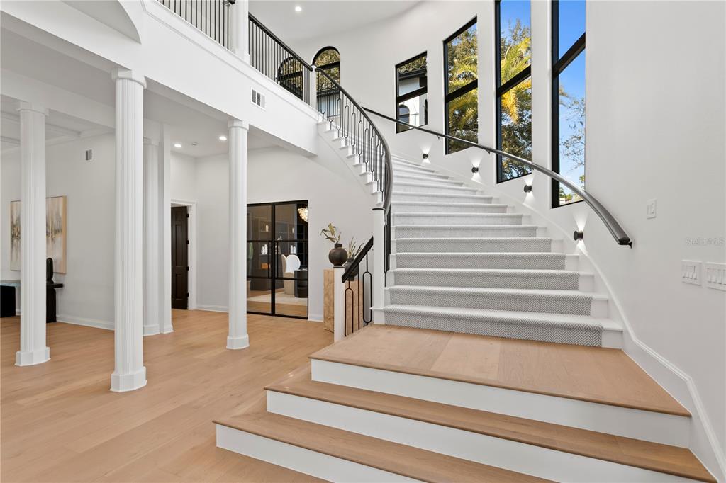 A grand foyer features a curved staircase with a patterned runner and light wood flooring — 6324 W MACLAURIN DRIVE, TAMPA, FL