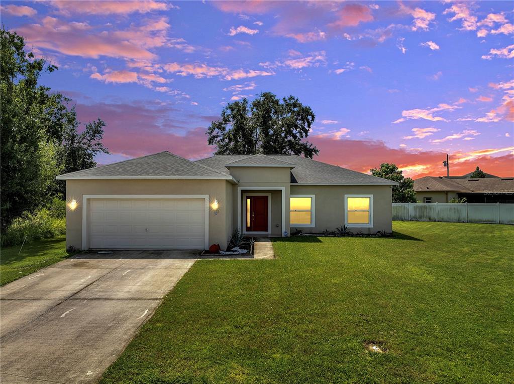 A single-story house with a two-car garage and a lawn under a sunset sky — 228 AMESBURY LANE, KISSIMMEE, FL