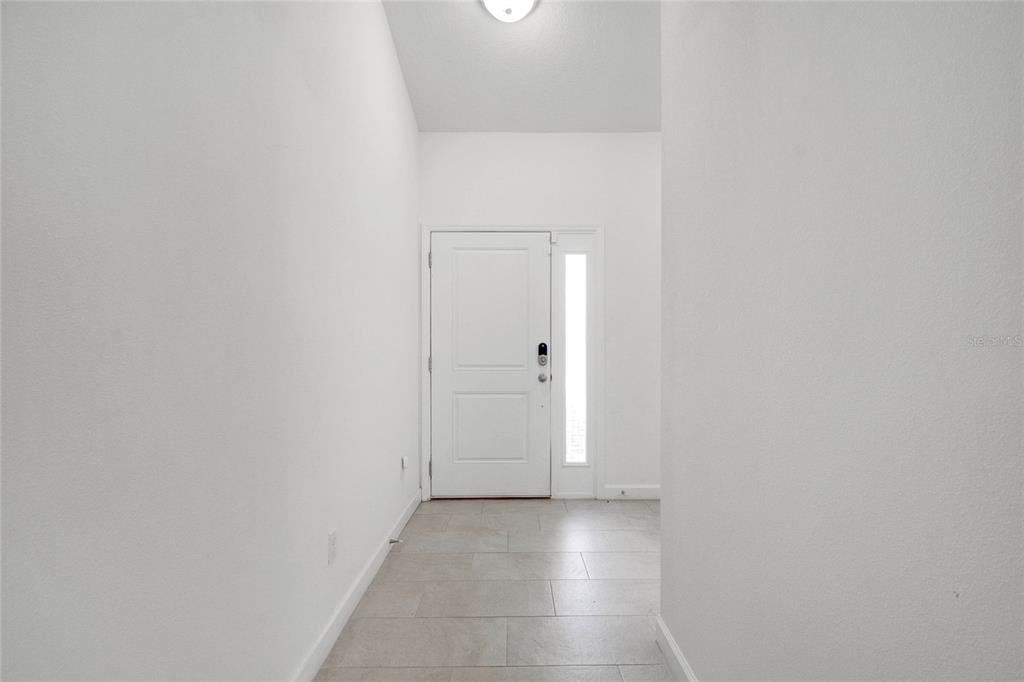 A bright entryway features white walls, tile flooring, and a white front door with sidelight — 228 AMESBURY LANE, KISSIMMEE, FL