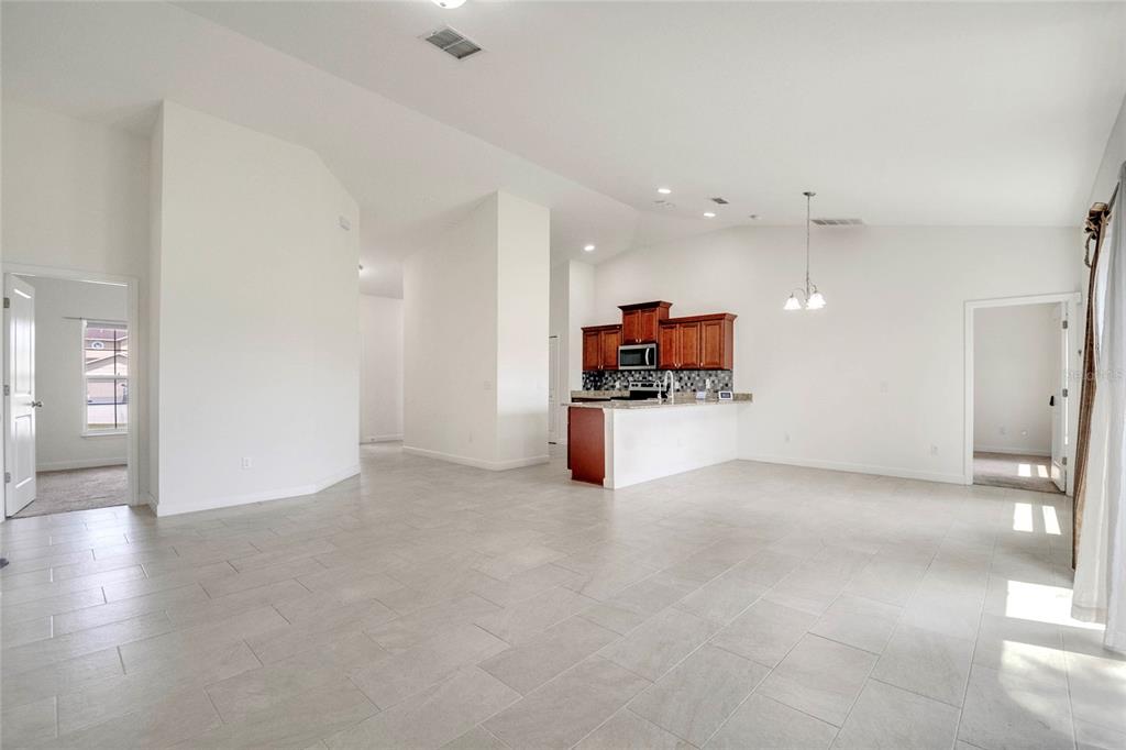 An open-concept living area features light tile flooring, white walls, and a kitchen with wood cabinets — 228 AMESBURY LANE, KISSIMMEE, FL