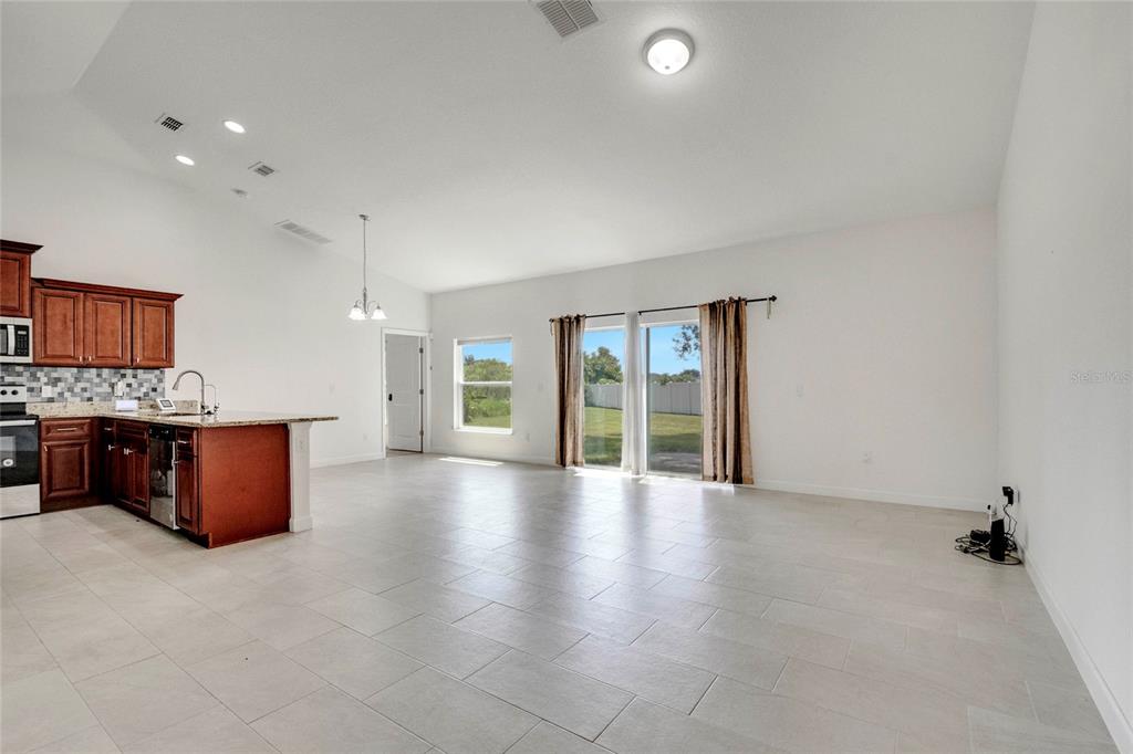 An open-concept kitchen and living area features tile flooring, dark wood cabinets, and sliding doors — 228 AMESBURY LANE, KISSIMMEE, FL