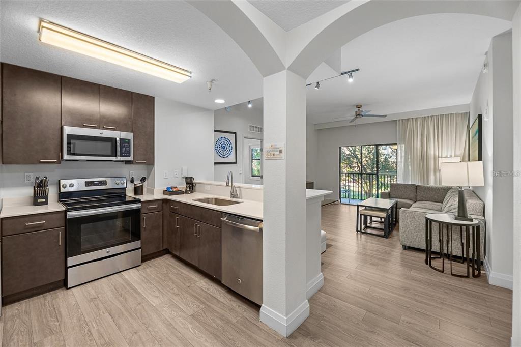 A kitchen with dark wood cabinets and stainless steel appliances opens to a living area — 14501 GROVE RESORT AVENUE UNIT 3406, WINTER GARDEN, FL