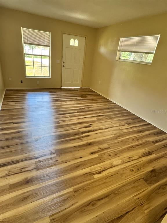 An empty room features light-colored wood-look flooring, a white entry door, and two windows — 128 11TH WAHNETA STREET W, WINTER HAVEN, FL
