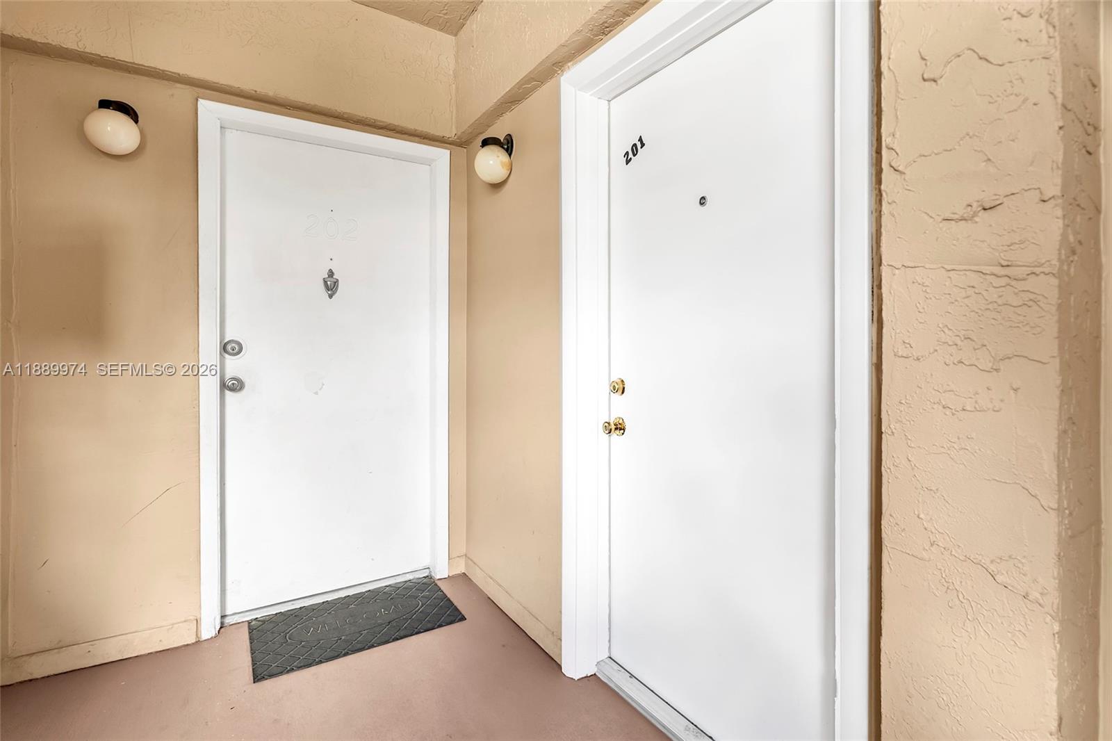 Two white apartment doors with unit numbers are set in a beige exterior hallway — 3945 SW 89th Ave # 201, Miami FL 33165, MIAMI, FL