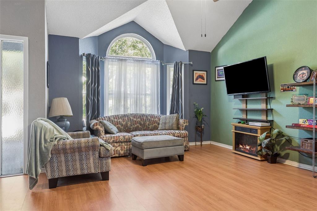 A living room with vaulted ceilings, wood-look flooring, a fireplace, and a patterned sofa — 3237 MONTROSE CIRCLE, PALM HARBOR, FL