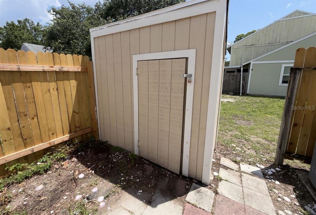 A beige wooden storage shed stands in a backyard next to a wooden fence — 96 TOMOKA MEADOWS BOULEVARD, ORMOND BEACH, FL