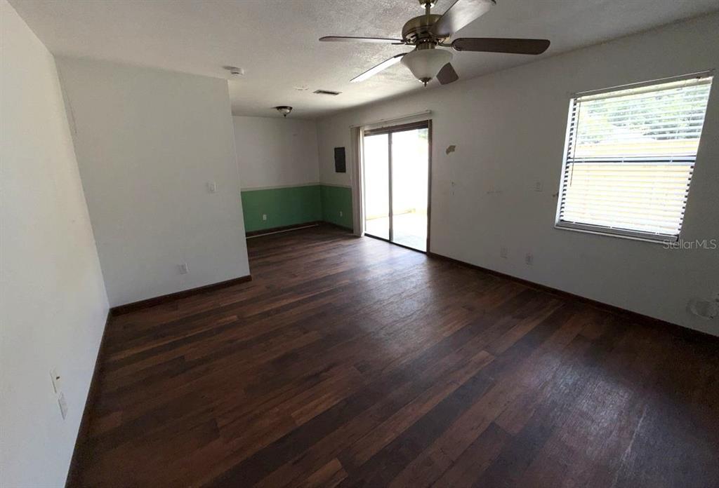 An empty living room features dark wood-look flooring, a ceiling fan, and a sliding glass door — 96 TOMOKA MEADOWS BOULEVARD, ORMOND BEACH, FL