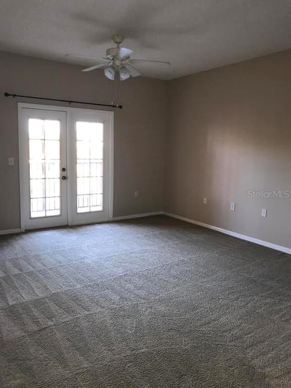 An empty room features beige walls, gray carpeting, a ceiling fan, and glass French doors — 10831 WINDSOR WALK DRIVE UNIT 1308, ORLANDO, FL