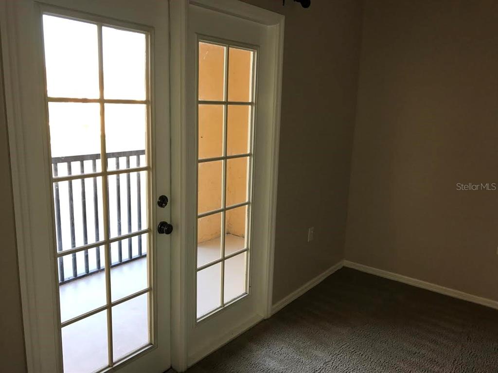 A room with gray carpet and a set of white French doors leading to a balcony — 10831 WINDSOR WALK DRIVE UNIT 1308, ORLANDO, FL