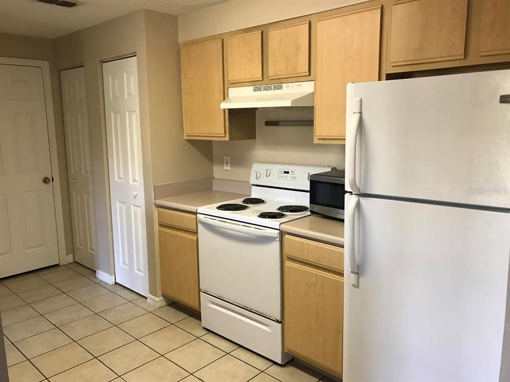 A kitchen features light wood cabinets, white appliances, and tiled flooring — 10831 WINDSOR WALK DRIVE UNIT 1308, ORLANDO, FL