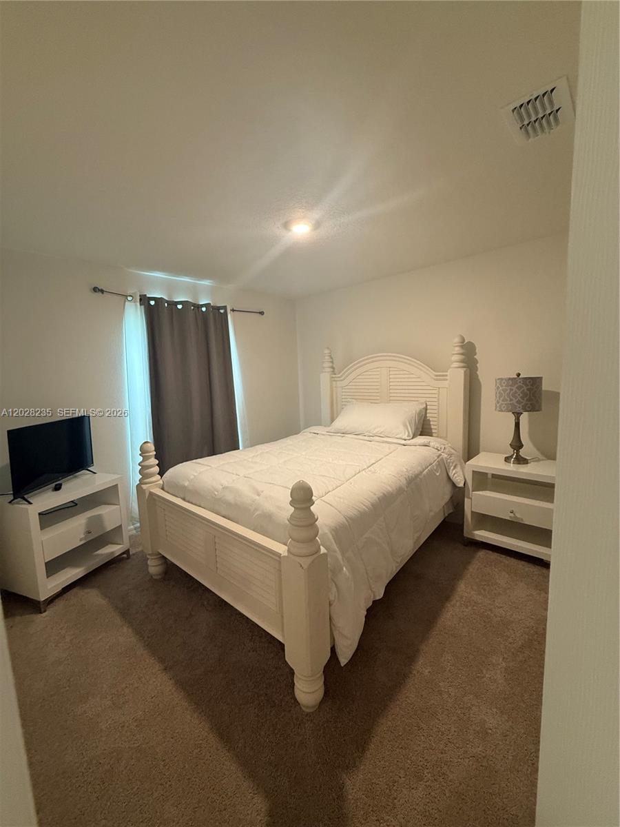A bedroom features a white bed frame, a matching nightstand, and a television on a stand — PORT ST. LUCIE, FL