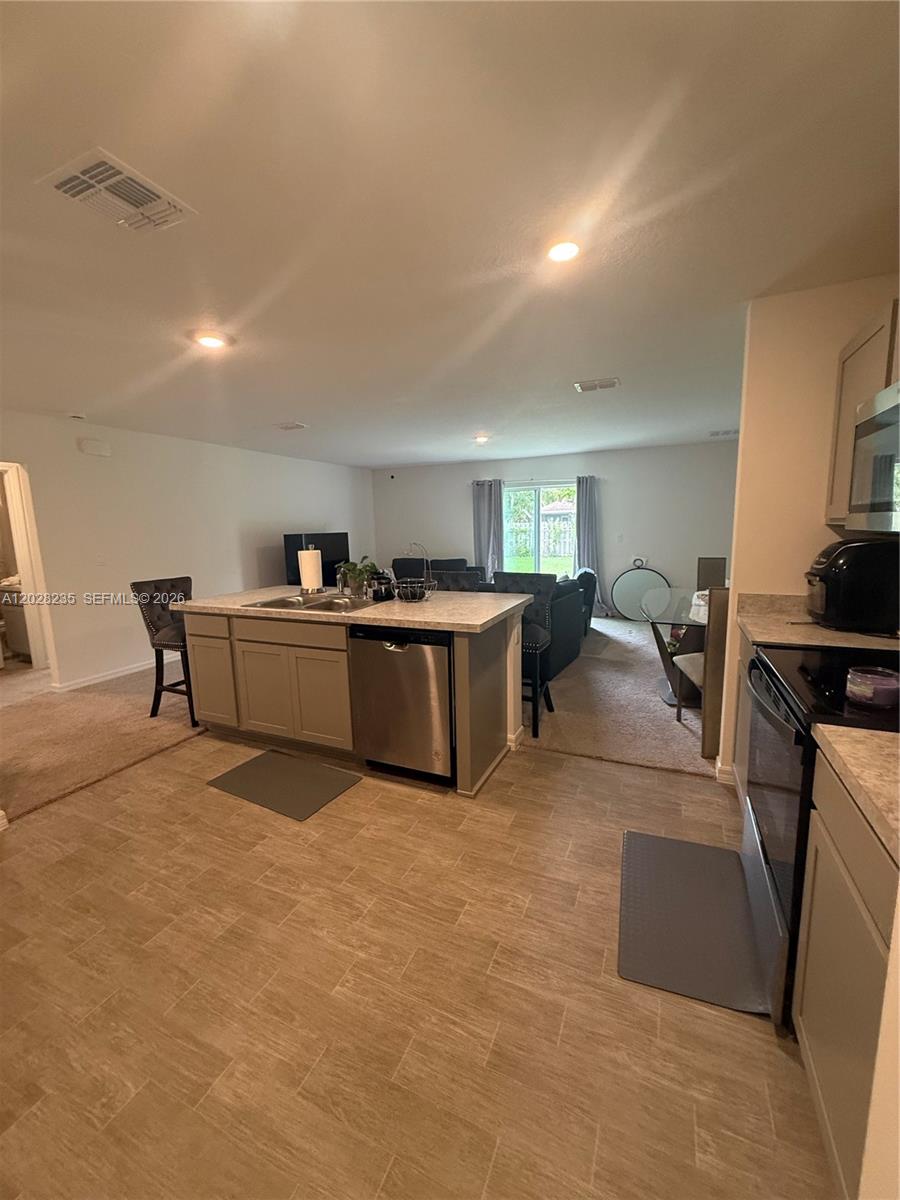 A kitchen with a central island and stainless steel appliances opens into a carpeted living area — PORT ST. LUCIE, FL