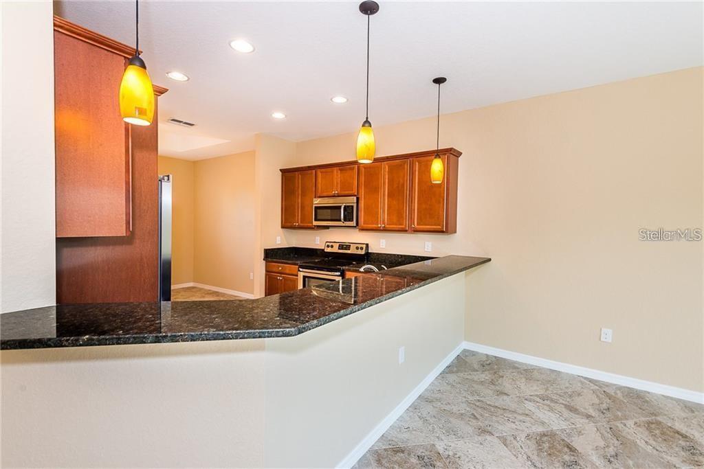 A kitchen features dark granite countertops, wood cabinets, stainless steel appliances, and three pendant lights — 3948 SAN ROCCO DRIVE UNIT 112, PUNTA GORDA, FL