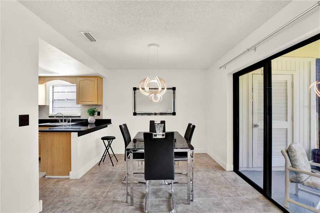 A dining area with a modern chandelier, black table set, and adjacent kitchen with wood cabinets — 20 SYLVIA PLACE, OLDSMAR, FL