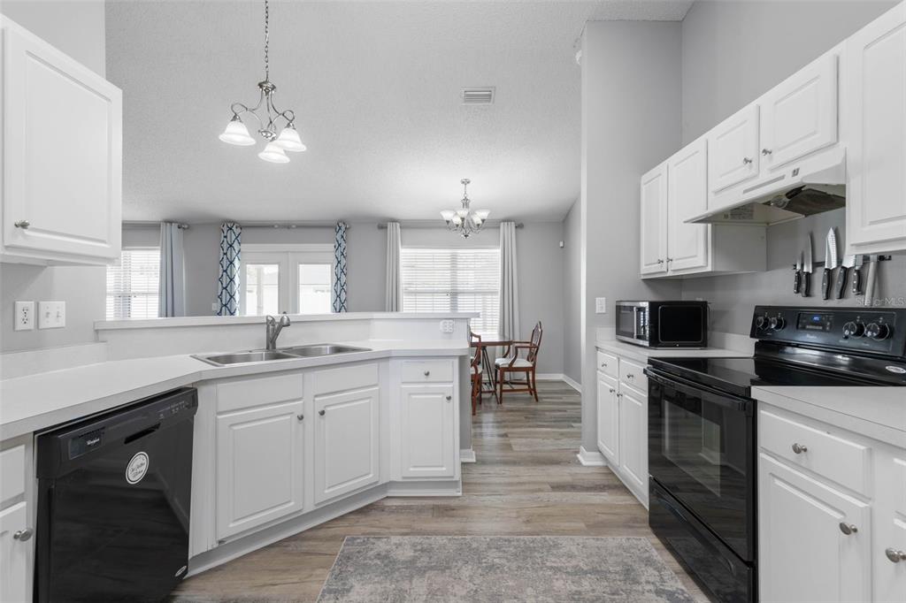 A kitchen with white cabinets, black appliances, and a breakfast bar overlooking a dining area — 34 FOREST GROVE DRIVE, PALM COAST, FL
