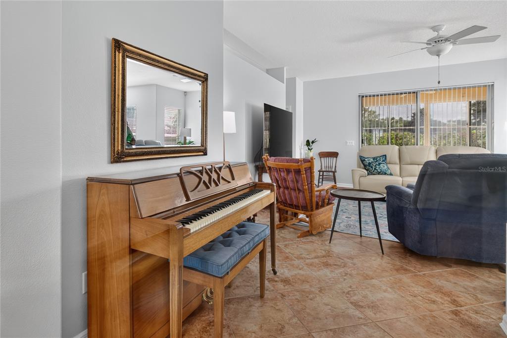 A living room features a wooden piano, tile flooring, a rocking chair, and a sofa — 4075 KINGSLEY STREET, CLERMONT, FL
