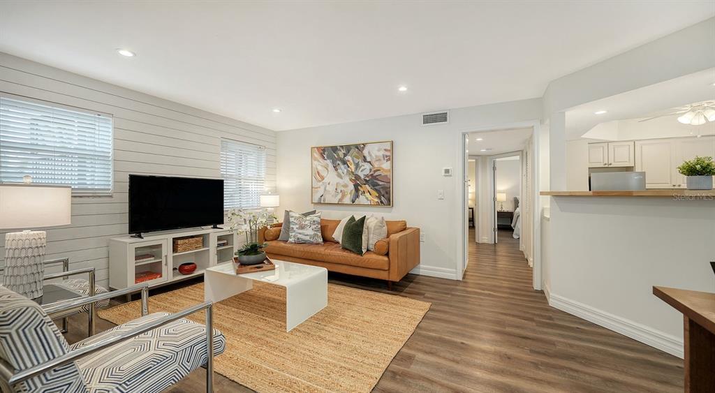 A living room features wood-look flooring, a tan leather sofa, and a white media console — 5610 AVENIDA DEL MARE, SARASOTA, FL