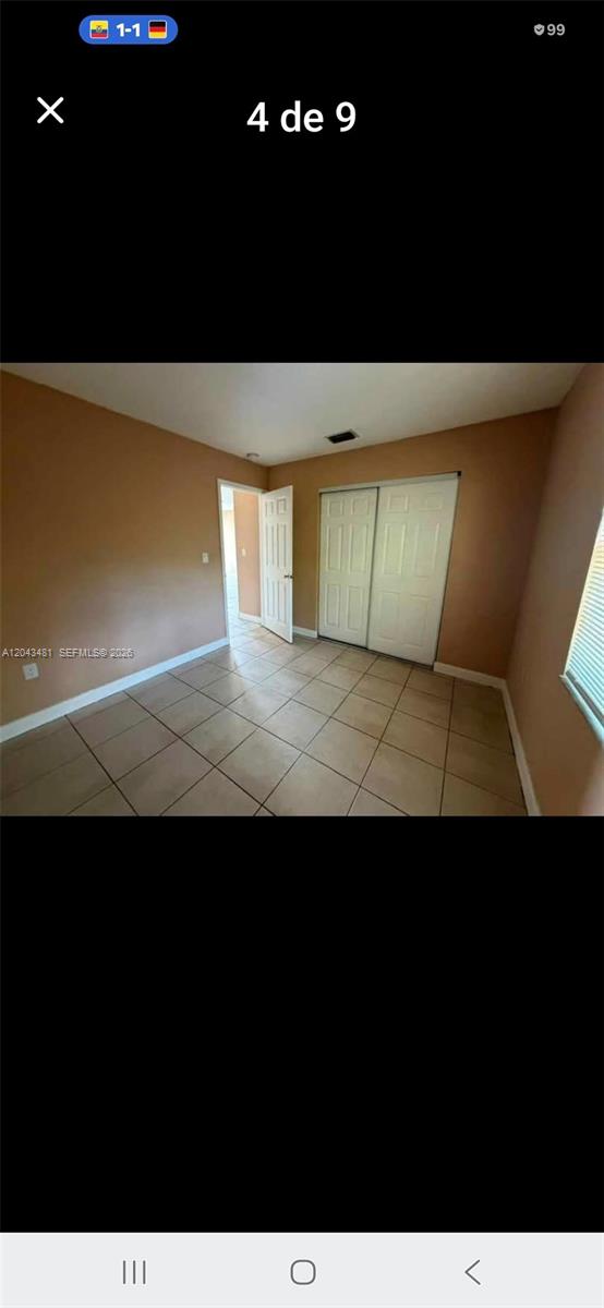 An empty bedroom features tan walls, tiled flooring, and a white sliding closet door — 244 NW 14th St # 1, Pompano Beach FL 33060, POMPANO BEACH, FL