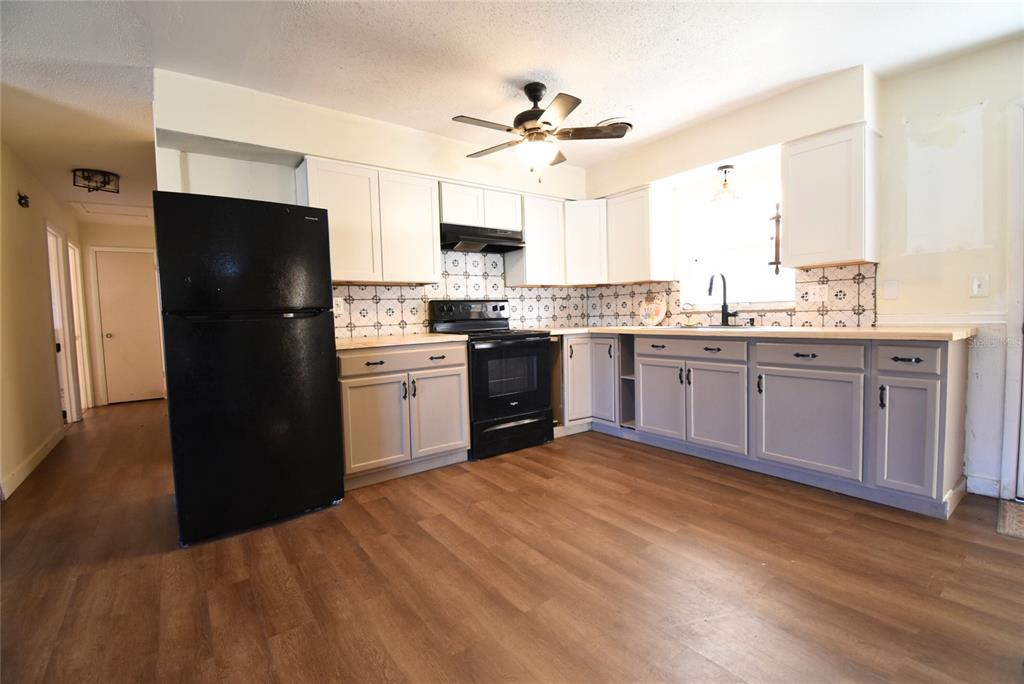 A kitchen features white upper cabinets, grey lower cabinets, black appliances, and wood-look flooring — 2810 NE 24TH AVENUE, OCALA, FL