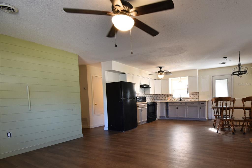 An open-concept kitchen and dining area featuring light wood flooring, a black refrigerator, and shiplap — 2810 NE 24TH AVENUE, OCALA, FL
