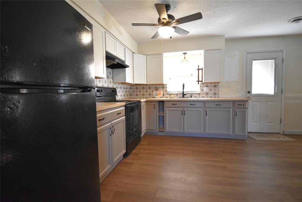 A kitchen features light gray lower cabinets, white upper cabinets, black appliances, and wood-look flooring — 2810 NE 24TH AVENUE, OCALA, FL