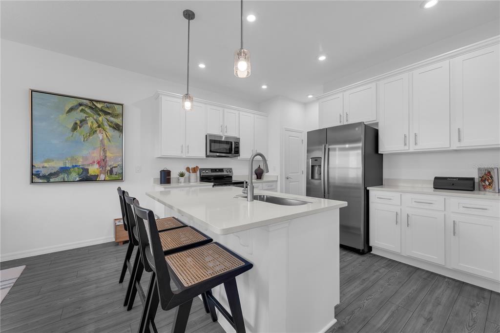 A modern kitchen features white cabinetry, a central island with bar seating, and stainless appliances — 10131 MORNING MEADOWLARK TRAIL, PARRISH, FL