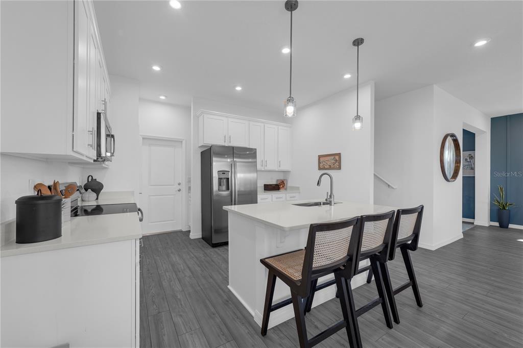 A modern kitchen features white cabinetry, a central island with bar stools, and gray flooring — 10131 MORNING MEADOWLARK TRAIL, PARRISH, FL