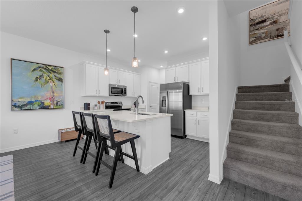 A modern kitchen features white cabinets, a central island with bar seating, and gray flooring — 10131 MORNING MEADOWLARK TRAIL, PARRISH, FL