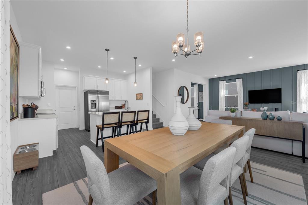 An open-concept dining area features a wooden table, light gray chairs, and a modern kitchen — 10131 MORNING MEADOWLARK TRAIL, PARRISH, FL
