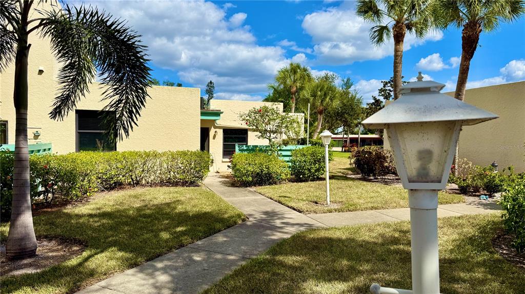 A concrete walkway leads to the entrance of a yellow stucco building with palm trees — 621 SPRING LAKES BOULEVARD UNIT 621, BRADENTON, FL