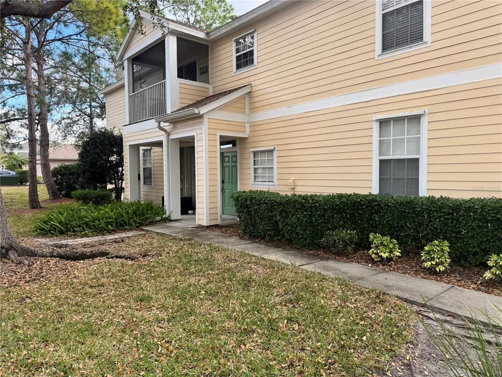 A light yellow two-story building features a green front door and a small patio area — 6315 ROSEFINCH COURT UNIT 101, LAKEWOOD RANCH, FL