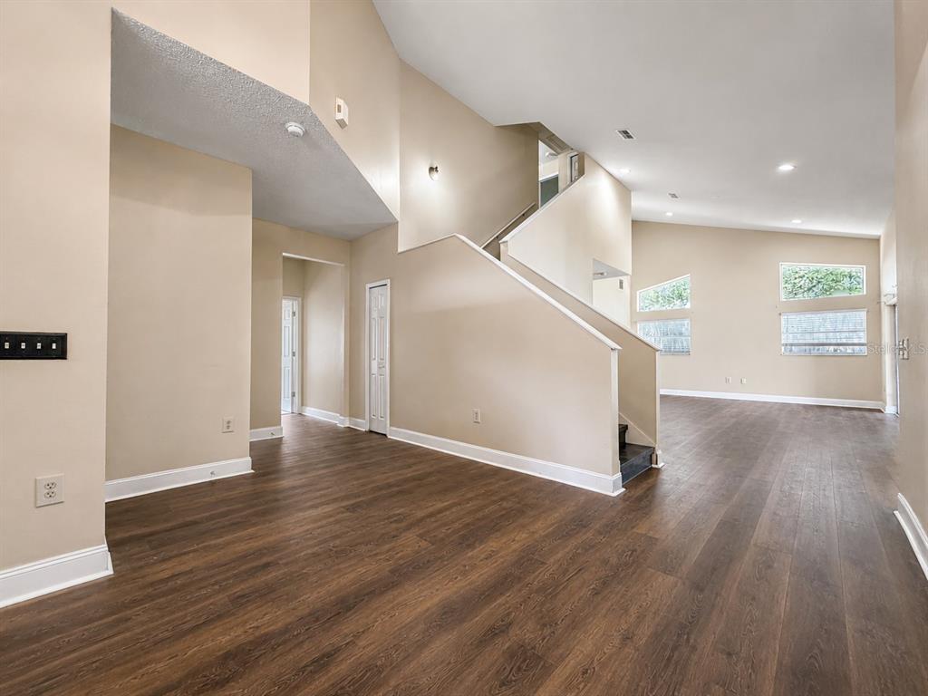An interior view shows a living area with wood-look flooring, beige walls, and a staircase — 114 WINCHESTER LANE, HAINES CITY, FL