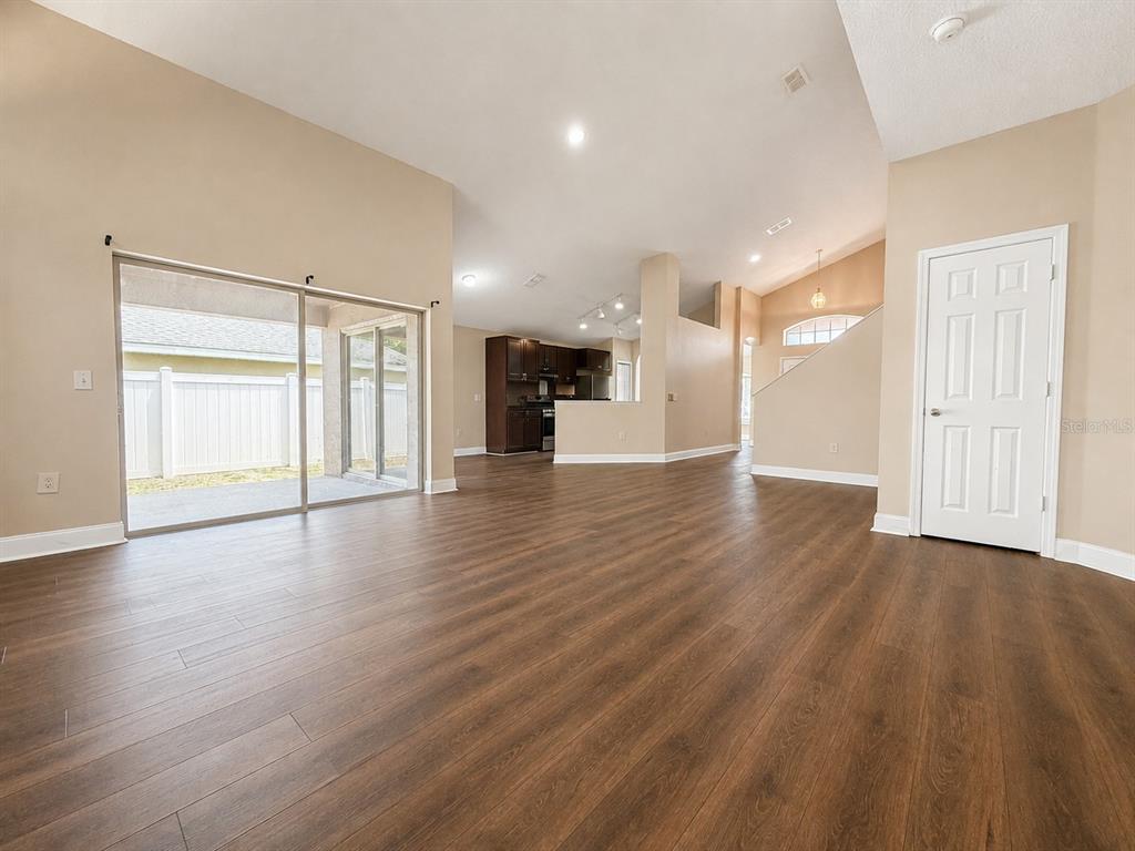 A spacious living area features wood-look flooring, high ceilings, a sliding glass door, and kitchen — 114 WINCHESTER LANE, HAINES CITY, FL