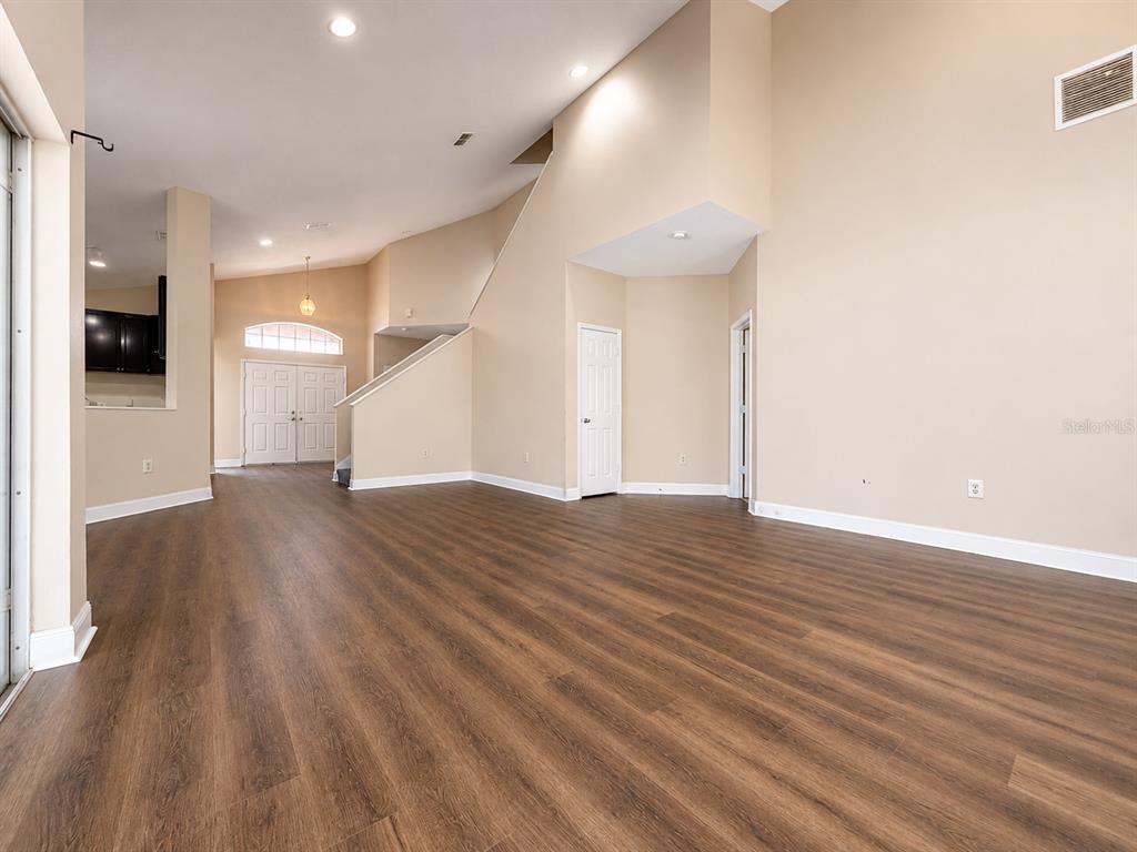 An empty living room features wood-look flooring, high ceilings, and a staircase — 114 WINCHESTER LANE, HAINES CITY, FL