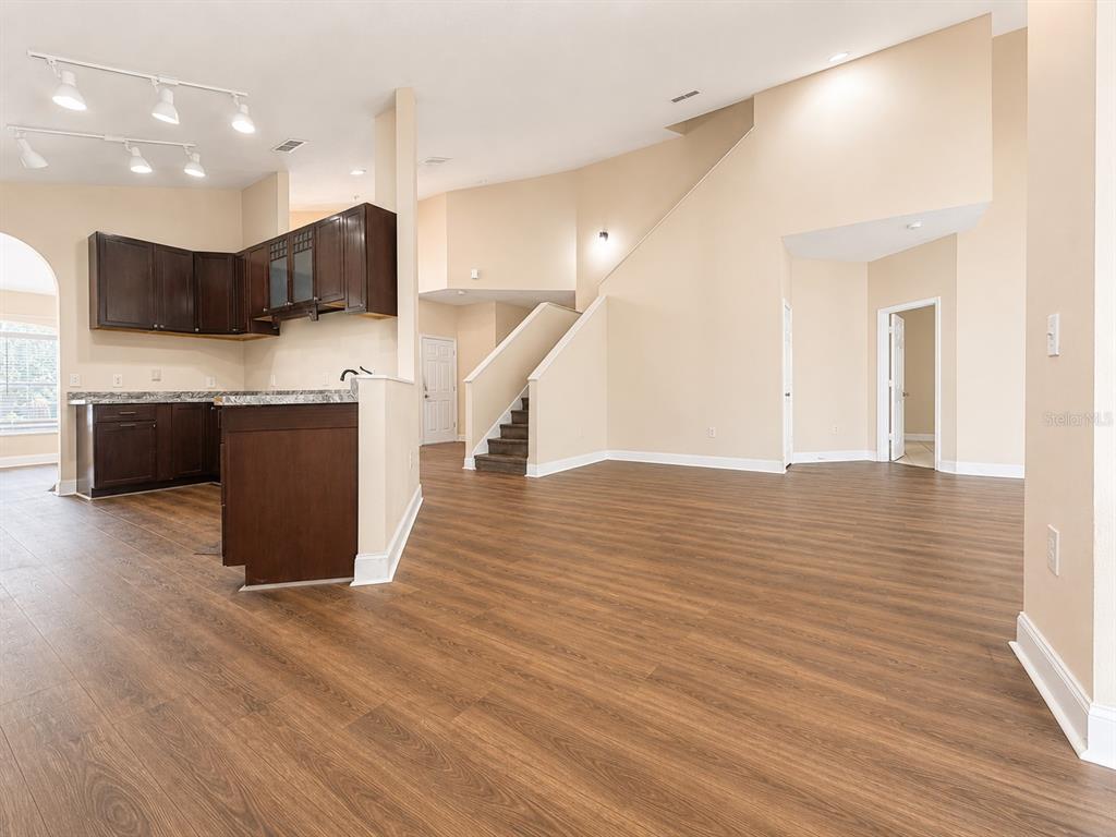 An open-concept living area features dark wood cabinets, laminate flooring, and a staircase — 114 WINCHESTER LANE, HAINES CITY, FL