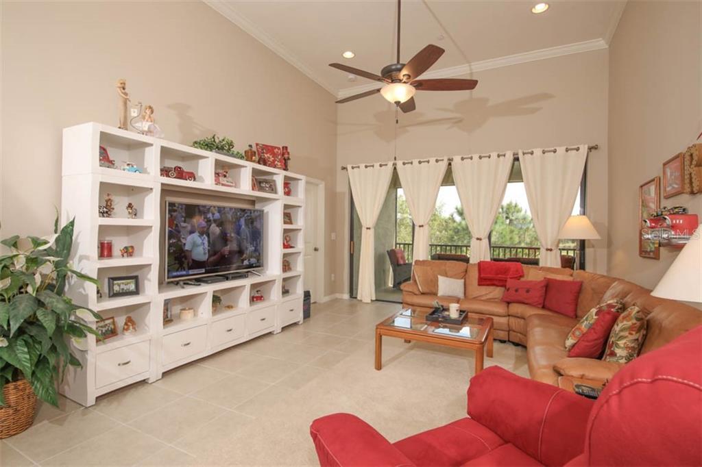 A living room features a large white entertainment center, a leather sectional, and sliding glass doors — 12720 SORRENTO WAY UNIT 201, BRADENTON, FL
