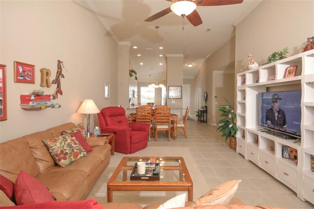 A living room with a tan leather sofa, red recliner, and white built-in media center — 12720 SORRENTO WAY UNIT 201, BRADENTON, FL