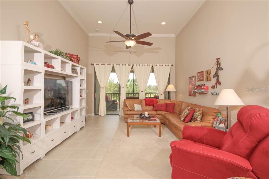A living room features a large white entertainment center, a leather sectional, and a red recliner — 12720 SORRENTO WAY UNIT 201, BRADENTON, FL