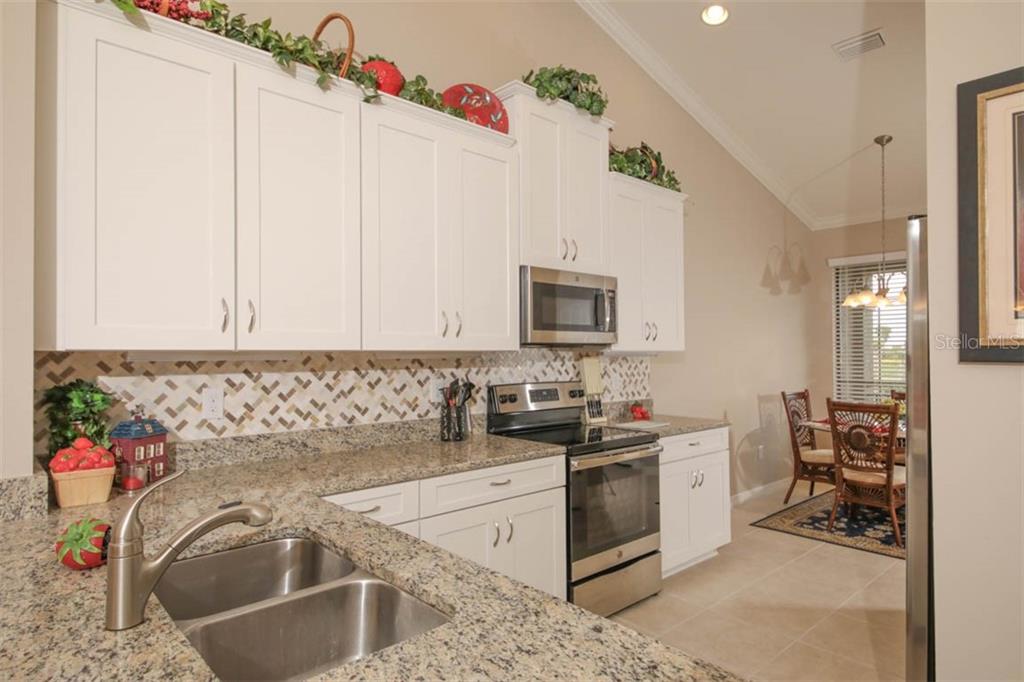 A kitchen features white cabinets, granite countertops, stainless steel appliances, and a tiled backsplash — 12720 SORRENTO WAY UNIT 201, BRADENTON, FL