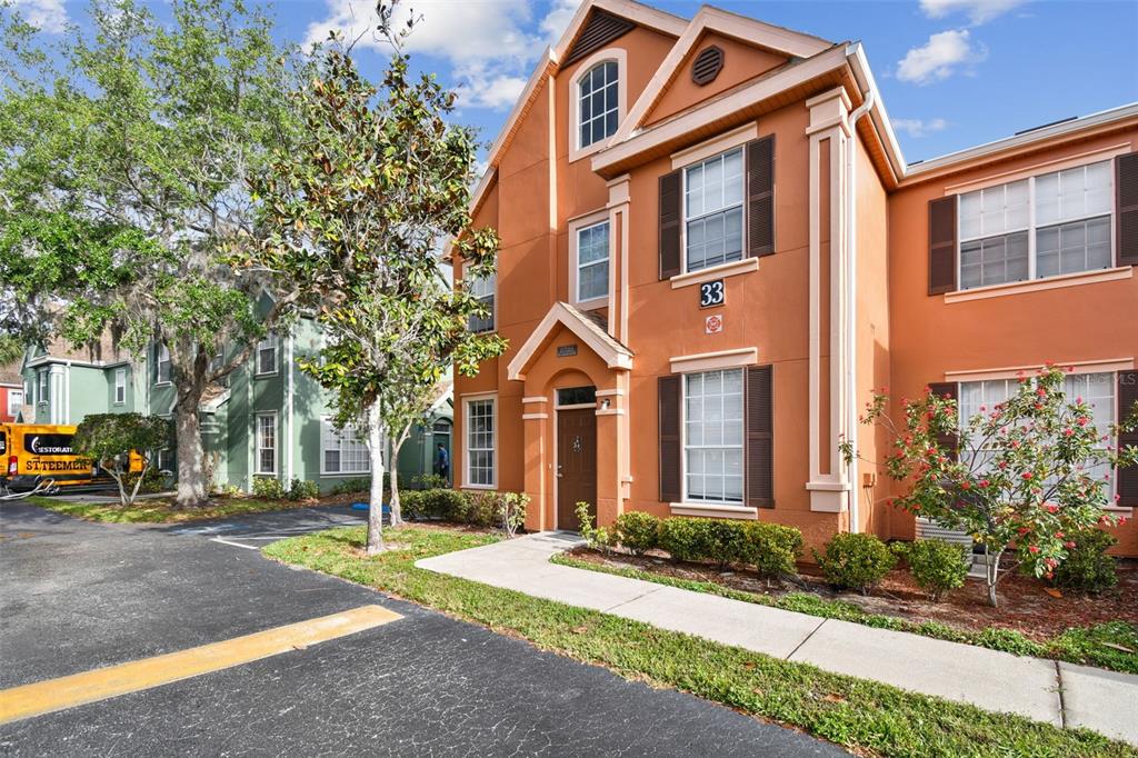 A three-story orange stucco townhouse with brown shutters and a front entrance walkway — 9740 LAKE CHASE ISLAND WAY UNIT 9740, TAMPA, FL