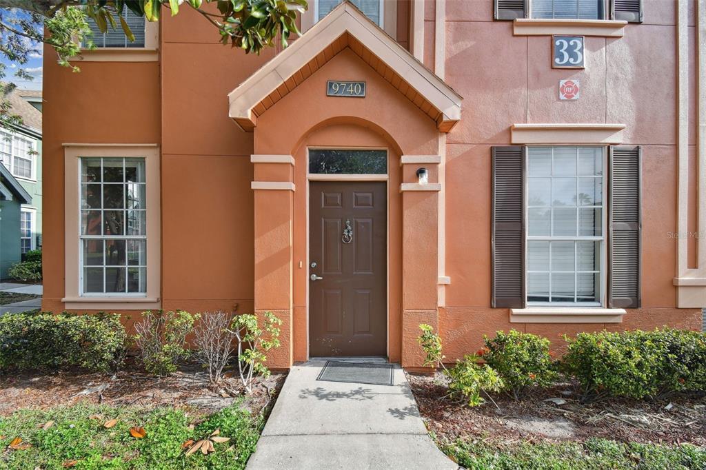 The exterior of a two-story orange stucco building features a brown front door and shutters — 9740 LAKE CHASE ISLAND WAY UNIT 9740, TAMPA, FL