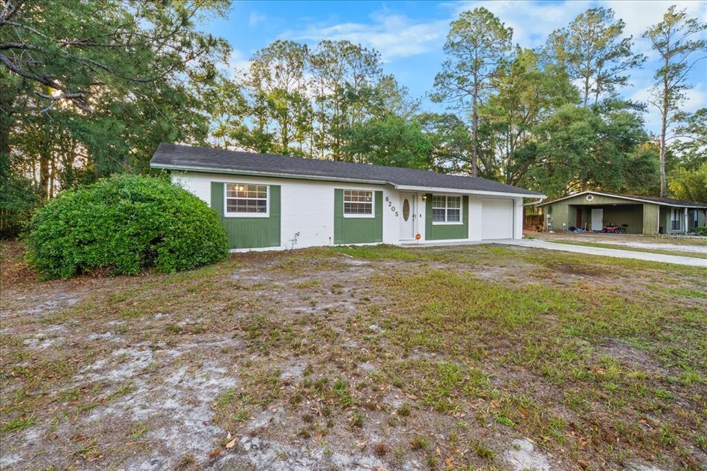 A single-story white house with green shutters and a garage sits on a grassy lot — 6205 NW 26TH TERRACE, GAINESVILLE, FL