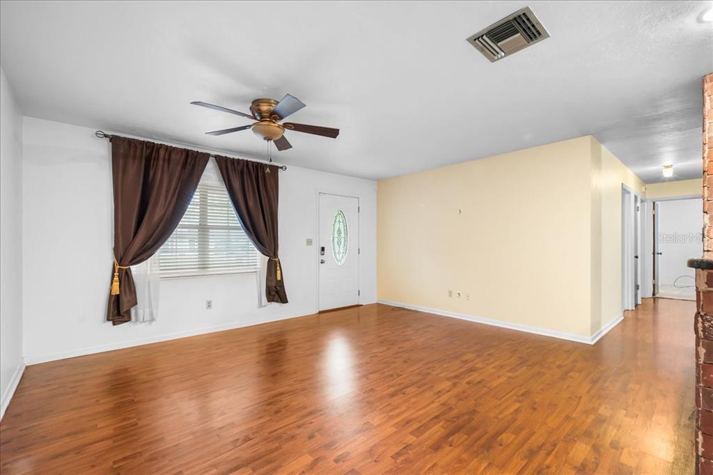 A living room with wood-look flooring, a ceiling fan, and a white front door — 6205 NW 26TH TERRACE, GAINESVILLE, FL