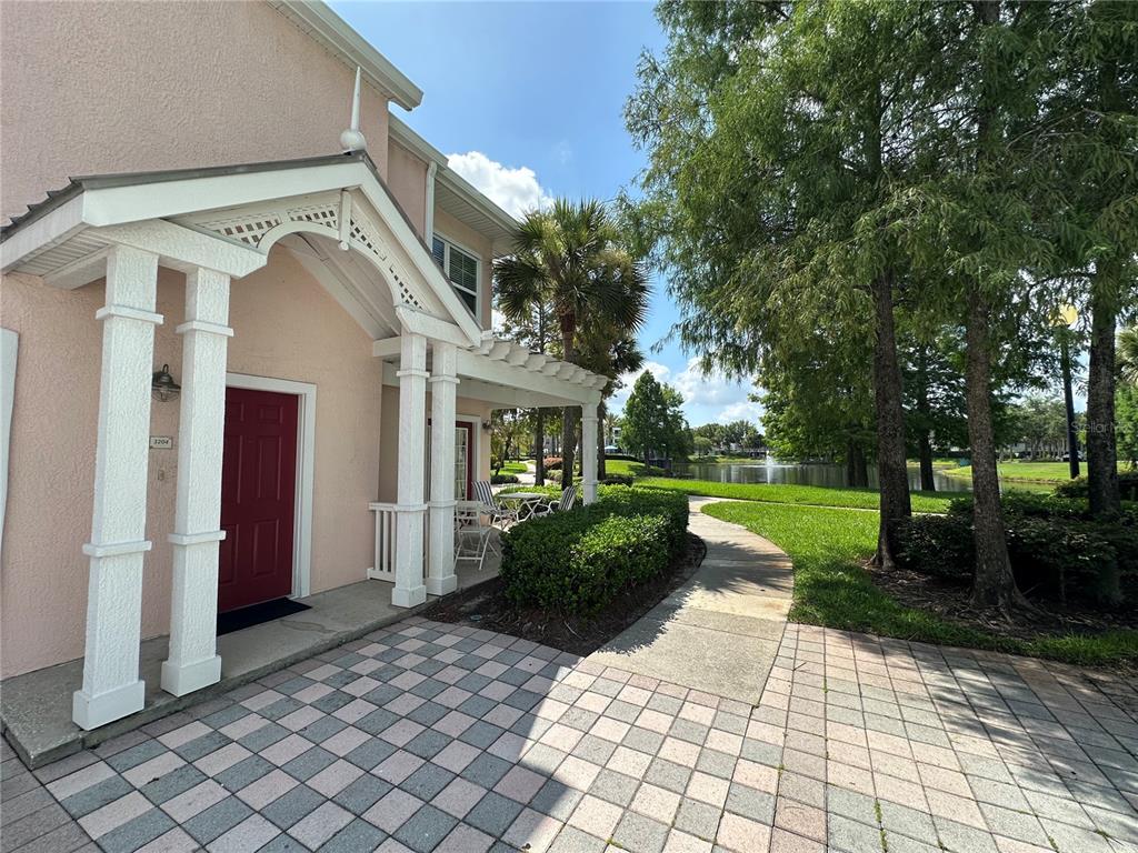 A pink building with a white porch and red door overlooks a pond and trees — 3006 BONFIRE BEACH DRIVE UNIT 204, KISSIMMEE, FL