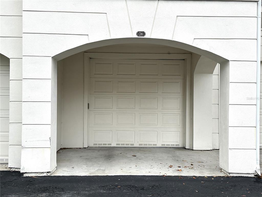 A white garage door is set within a recessed arched entryway of a stucco building — 12843 MADISON POINTE CIRCLE UNIT 201, ORLANDO, FL
