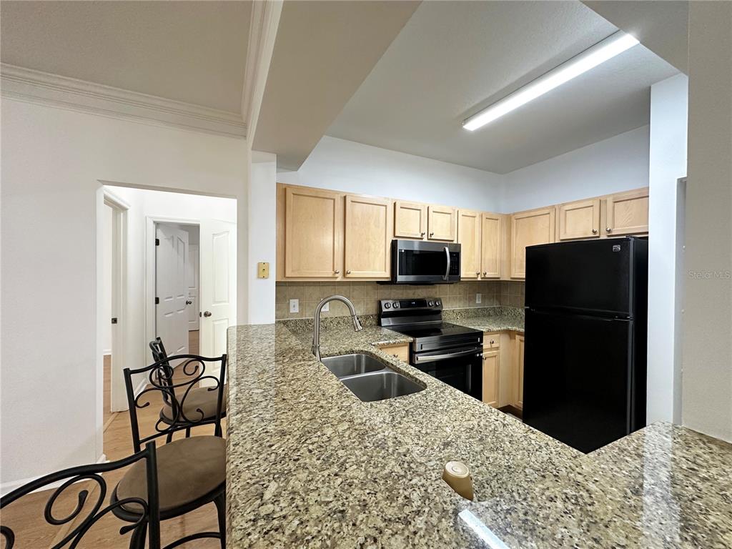 A kitchen features light wood cabinets, granite countertops, a black refrigerator, and a breakfast bar — 12843 MADISON POINTE CIRCLE UNIT 201, ORLANDO, FL
