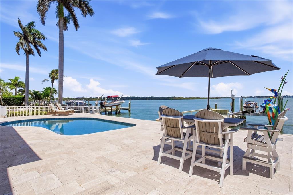 A patio with a pool, outdoor dining set, and umbrella overlooks a waterfront boat dock — 547 JOHNS PASS AVENUE, MADEIRA BEACH, FL