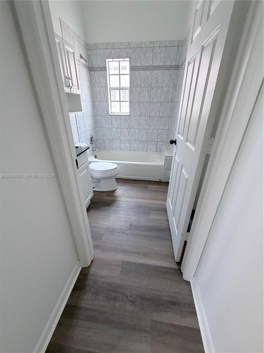 A bathroom features wood-look flooring, a white vanity, a toilet, and a tiled tub surround — 1657 Tyler St # 207, Hollywood FL 33020, HOLLYWOOD, FL