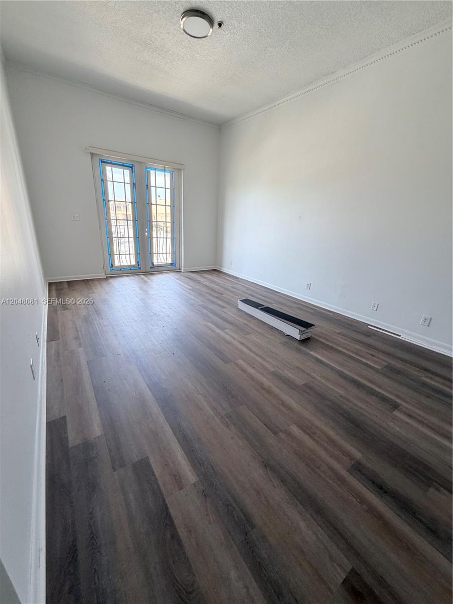An empty room features wood-look flooring, white walls, and a set of glass French doors — 1657 Tyler St # 207, Hollywood FL 33020, HOLLYWOOD, FL